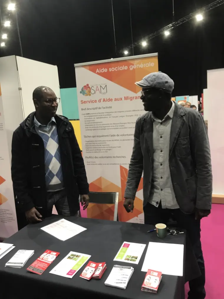 Deux hommes devant le stand d'aide sociale générale, lors d'un salon.