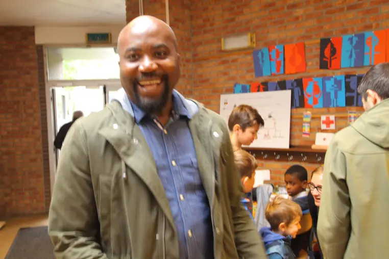 Un homme souriant lors d'une rencontre, dans une salle animée.