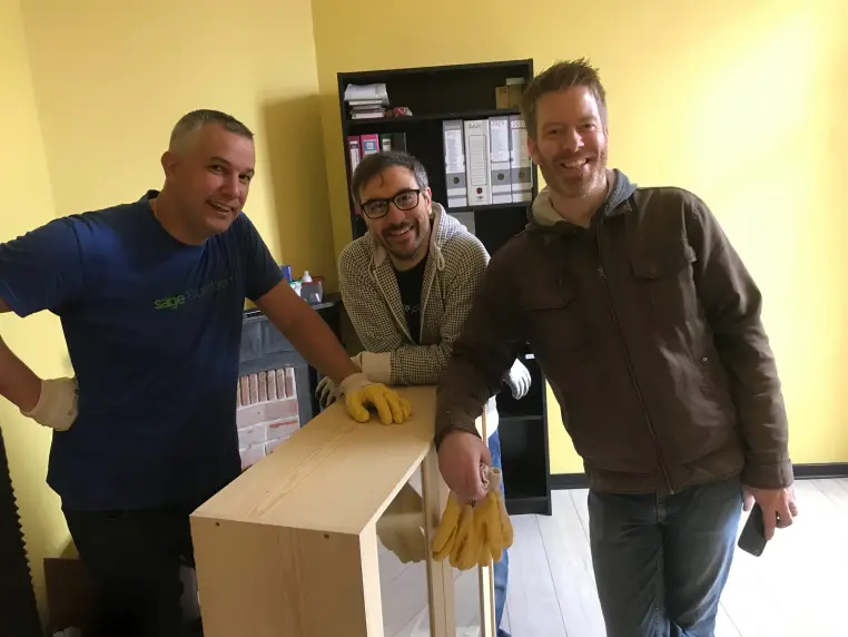 Trois hommes portent un carton de dons matériels.