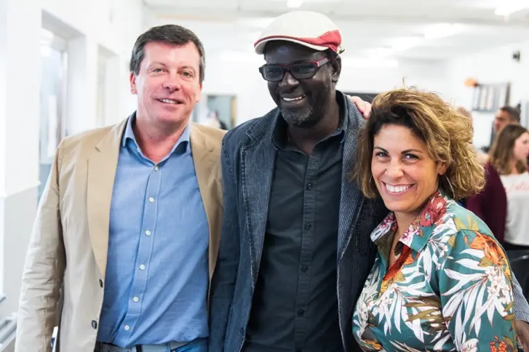 Trois personnes souriantes côte à côte, dans un espace de travail.